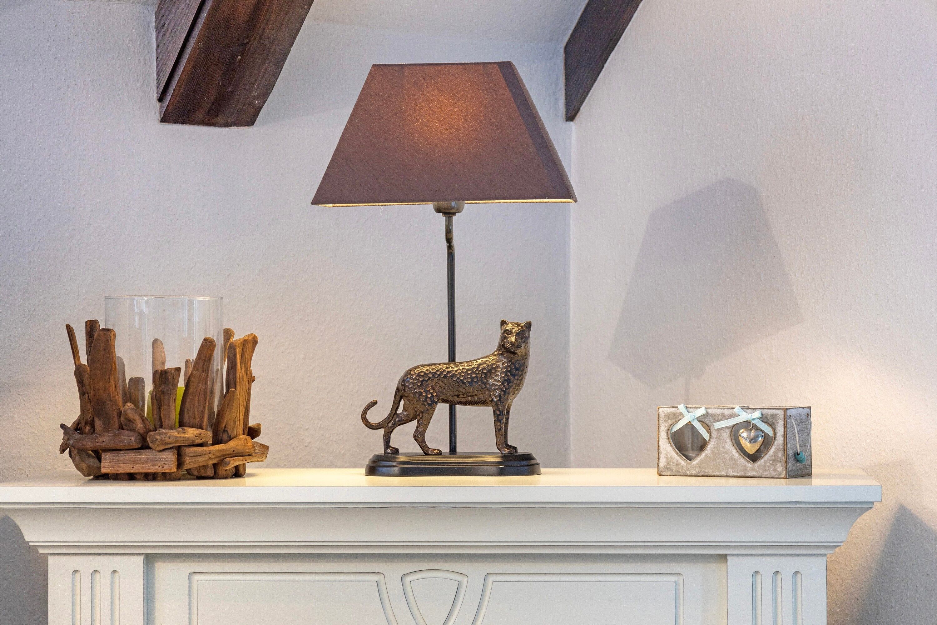 A fireplace mantel with a lamp, a decorative cat figurine, and a heart-shaped box.