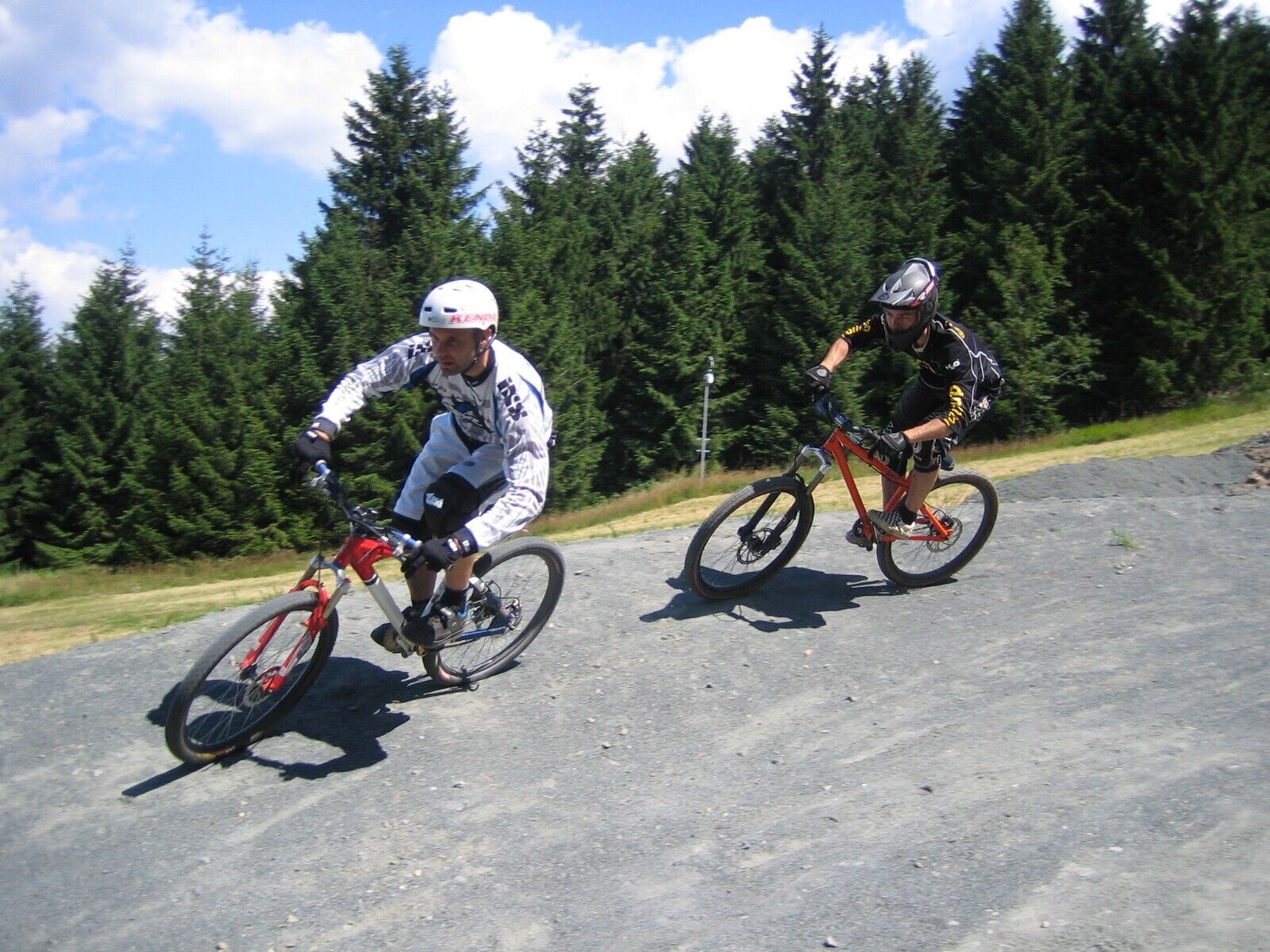Two cyclists on a paved road with a forest in the background.