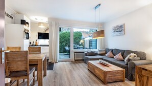 A modern living room with a sofa, coffee table, and dining area with chairs and a table. - Apartment 'Schönes Leben 4' with Sauna, Shared Terrace & Garden (Goslar)