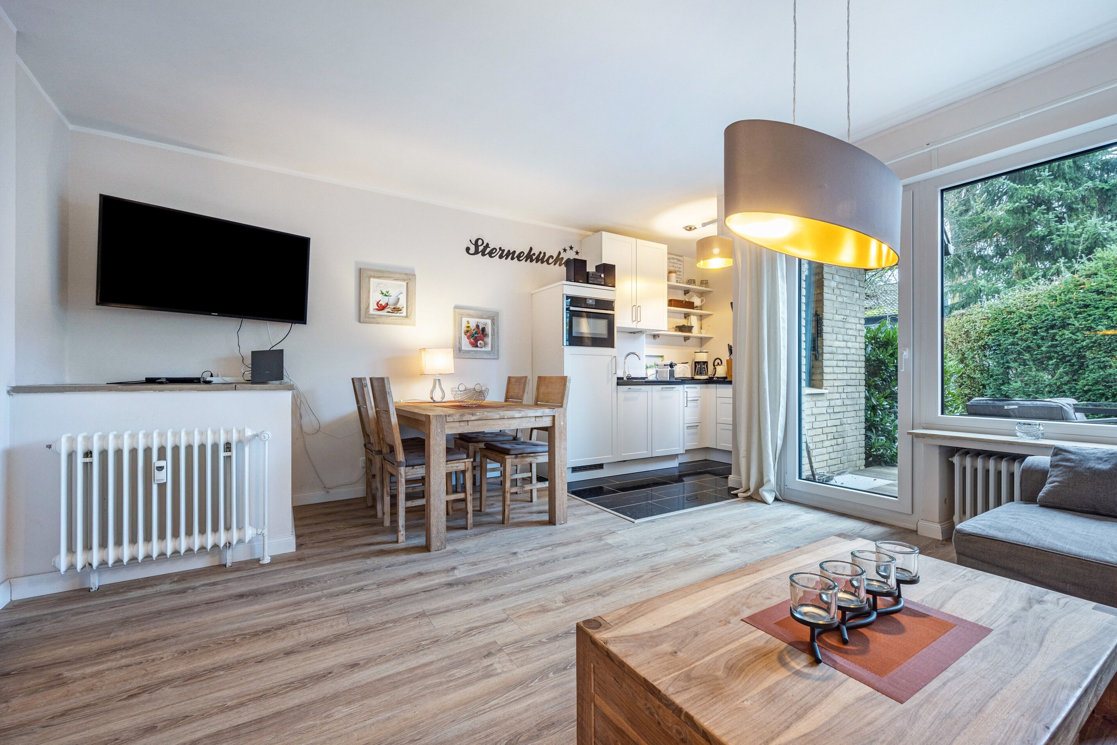 Un salon moderne doté d’un téléviseur, d’un coin repas, d’une cuisine et de grandes fenêtres.