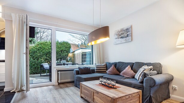 A modern living room with a sectional sofa, a wooden coffee table, and a large window with a view of the outdoors. - Apartment 'Schönes Leben 4' with Sauna, Shared Terrace & Garden (Goslar)