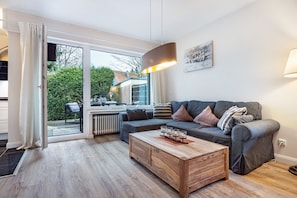 Un salon moderne avec un canapé d’angle, une table basse en bois et une grande fenêtre donnant sur l’extérieur.