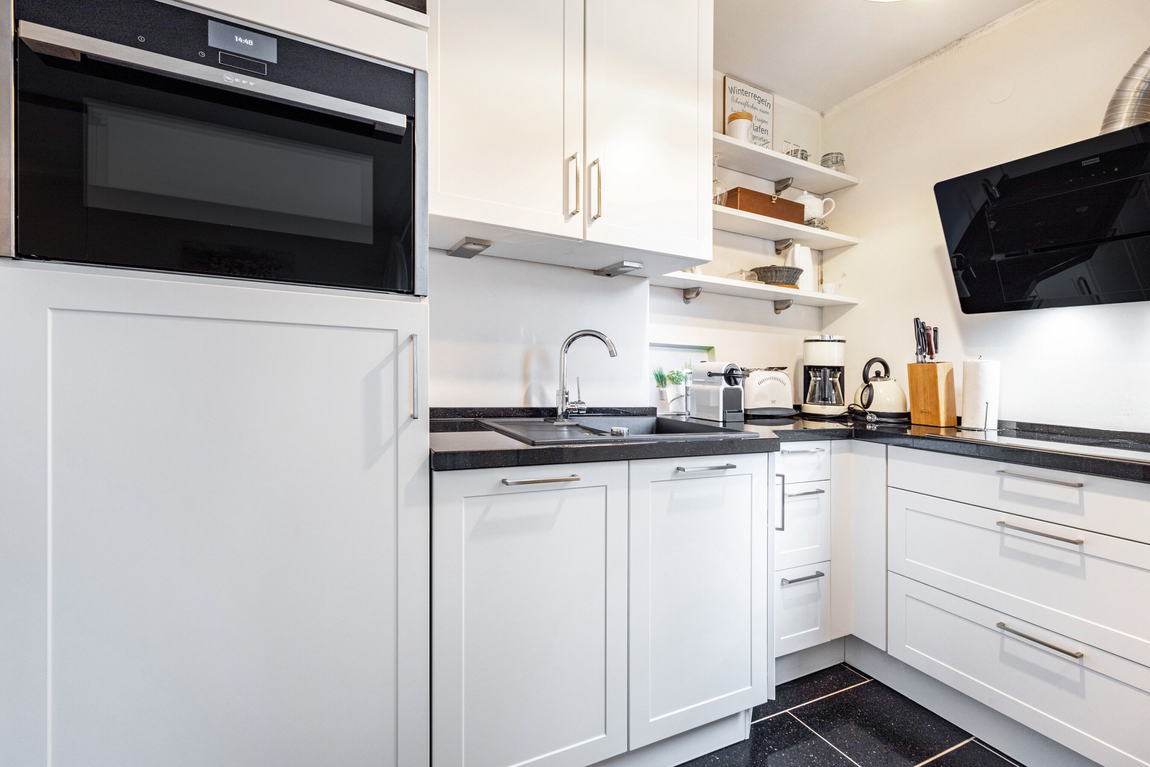 Una cocina moderna con armarios blancos, horno empotrado, lavaplatos y un televisor de pantalla plana montado en la pared.