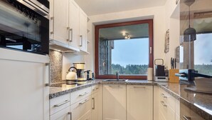A modern kitchen with white cabinets, granite countertops, and a large window offering a view of the outdoors.