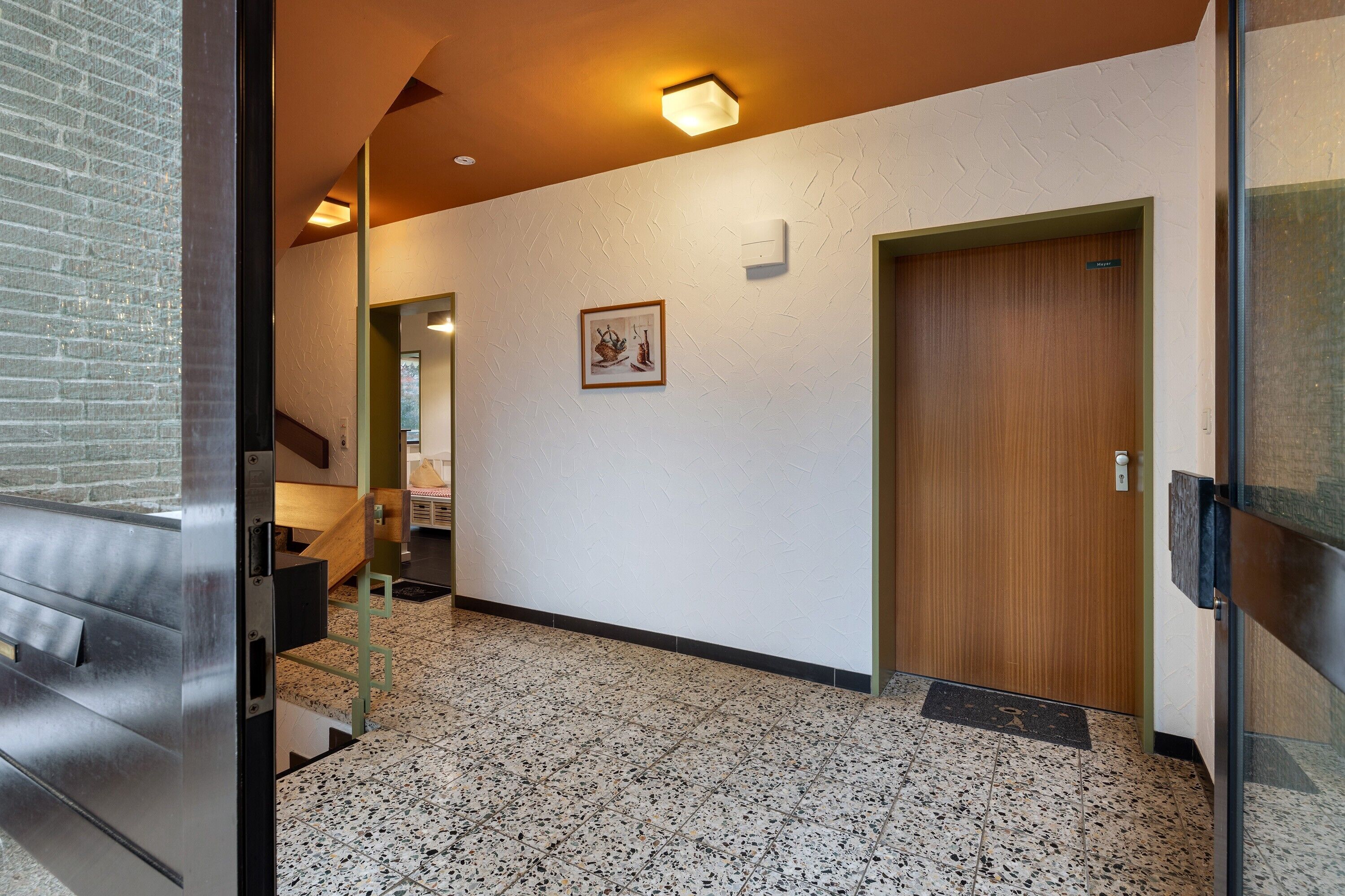 Un pasillo con una puerta de madera, un cuadro en la pared y una escalera que conduce a otra habitación.