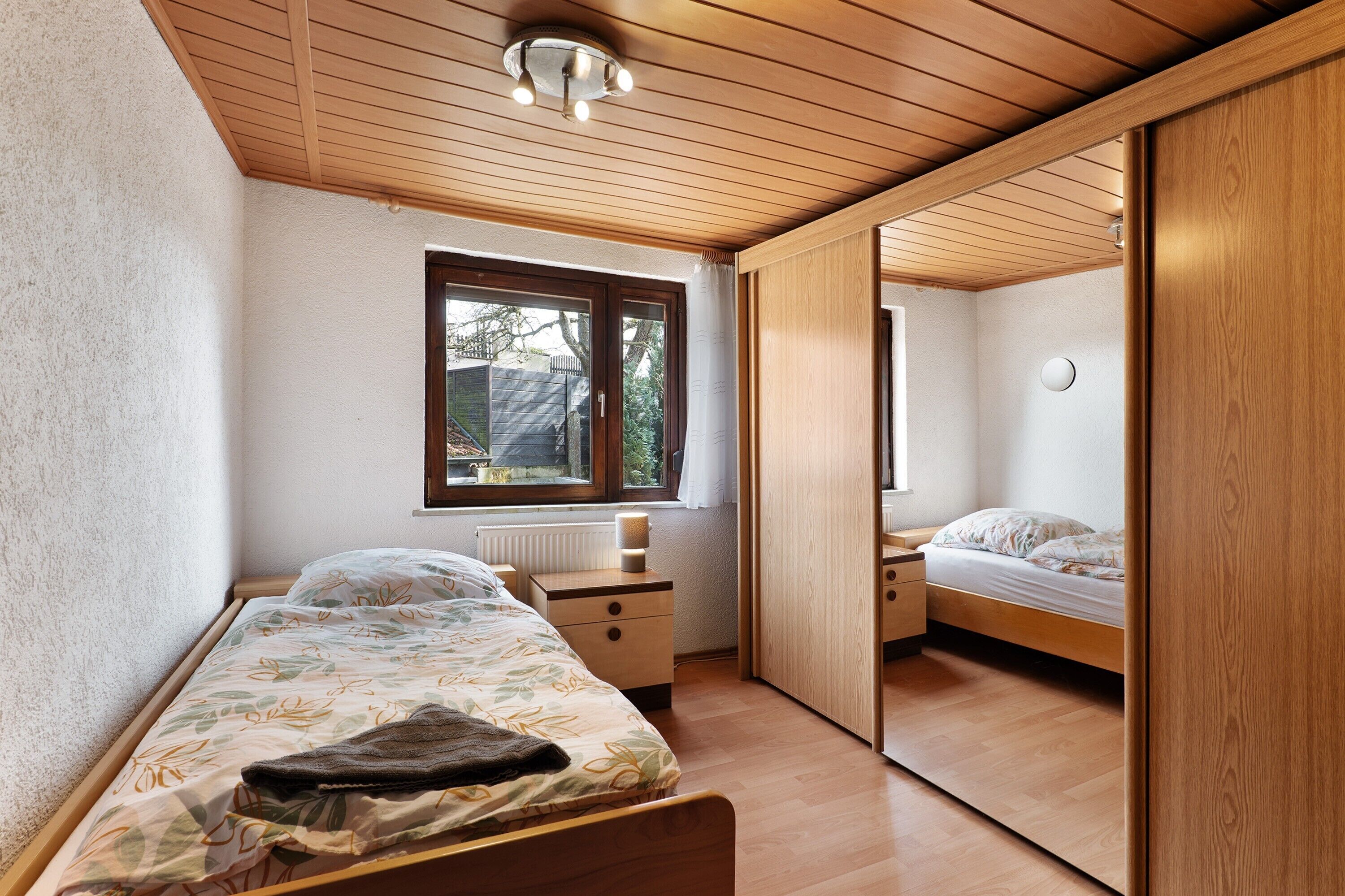 A bedroom with a bed, a nightstand, a window, and a wardrobe.