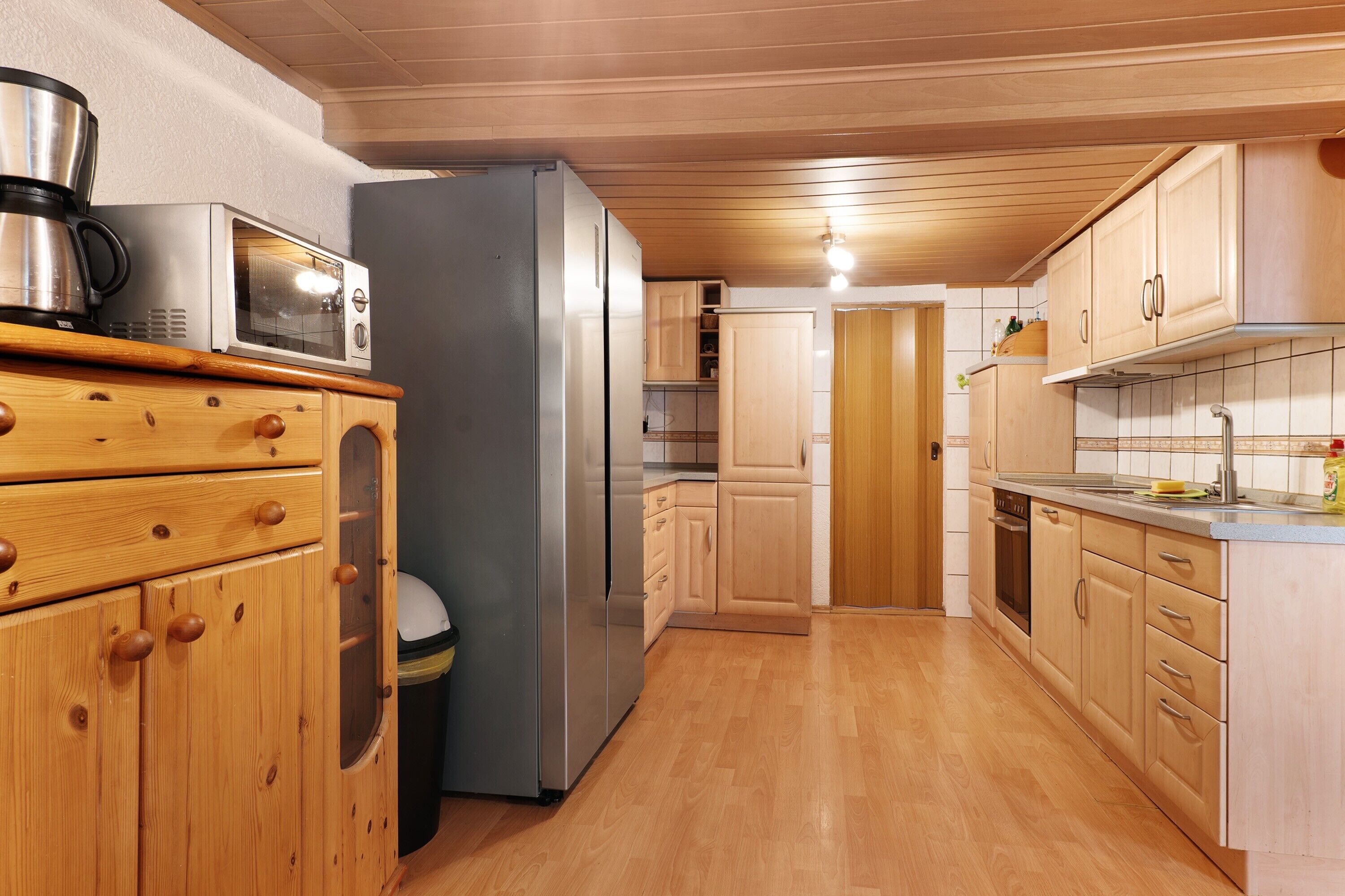 A compact kitchen with wooden cabinets, a stainless steel refrigerator, a microwave, and a coffee maker.
