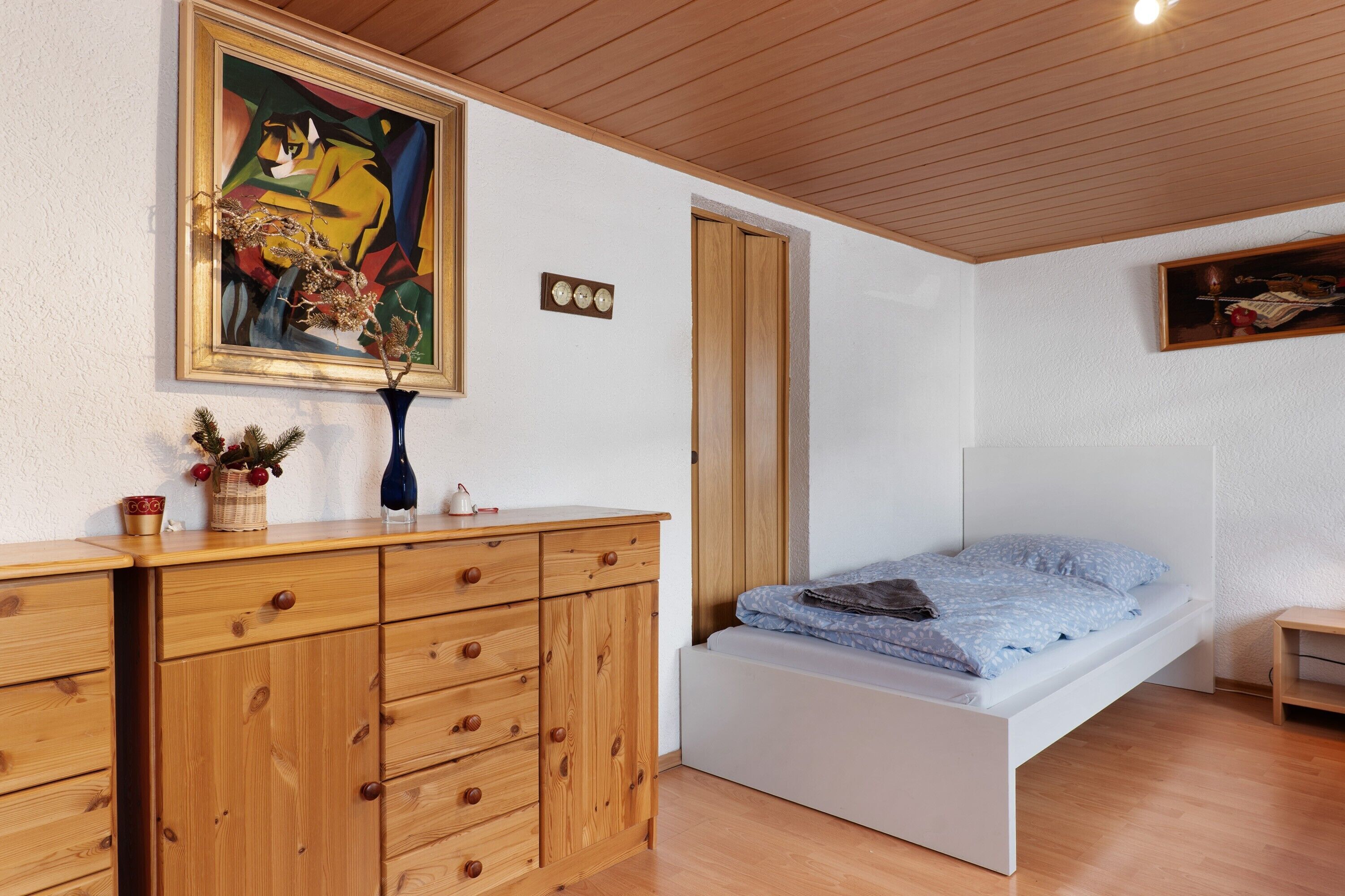 Ein Zimmer mit einem Bett, einem Holzschrank und zwei Bildern an den Wänden.