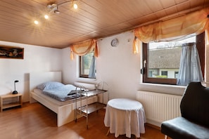 A room with a bunk bed, a small table, a chair, a radiator, and a window with curtains.