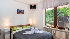 A bedroom with a bed, bedside lamps, a radiator, a window with a view of greenery, and a painting on the wall. - Apartment 'Zwergenbau' with Shared Garden, Balcony, and Wi-Fi (Badenweiler)