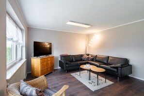 A modern living room with a flat-screen TV on a wooden cabinet, a leather sofa, a round coffee table, and a floor lamp.