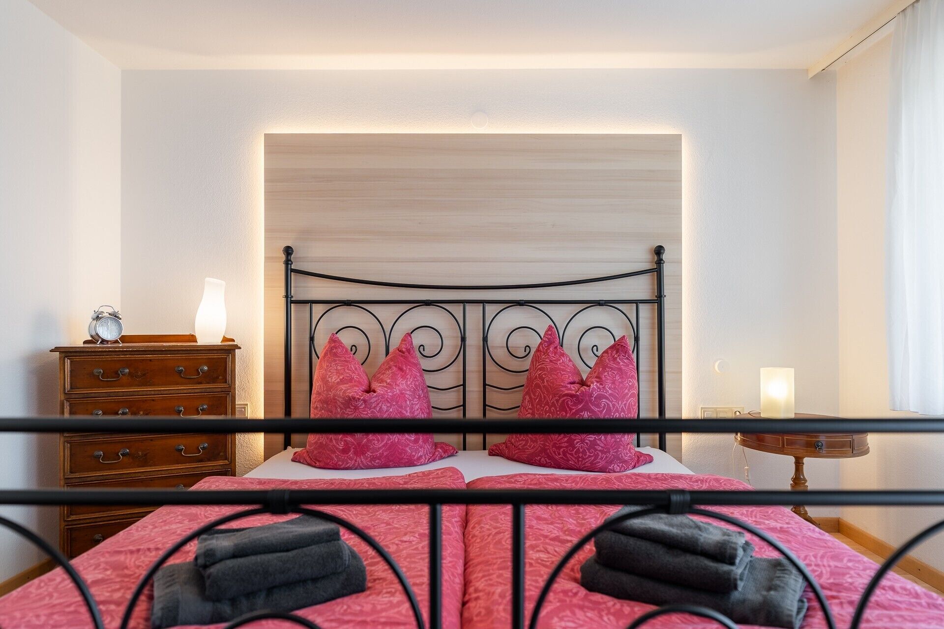 A bedroom with a bed, a nightstand, a dresser, and a wall-mounted light.