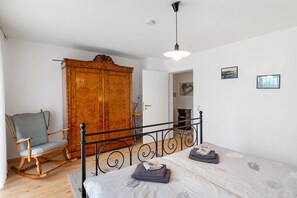 Une chambre à coucher comprenant un lit, un fauteuil à bascule, une armoire et une porte donnant sur une autre pièce.