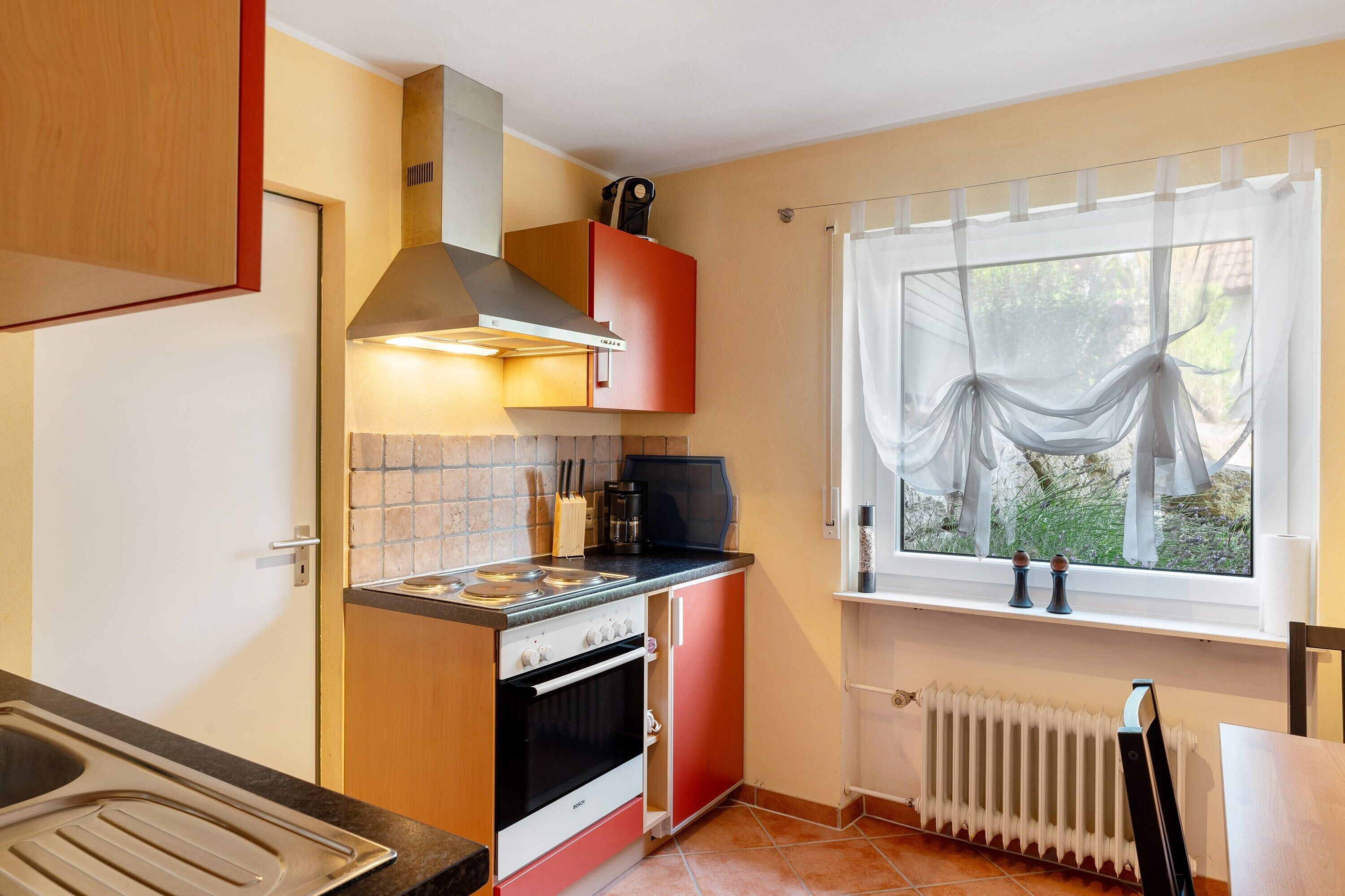 Una cocina compacta con estufa, horno y ventana con cortinas traslúcidas.