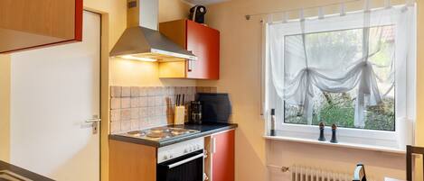 Una cocina compacta con estufa, horno y ventana con cortinas traslúcidas.