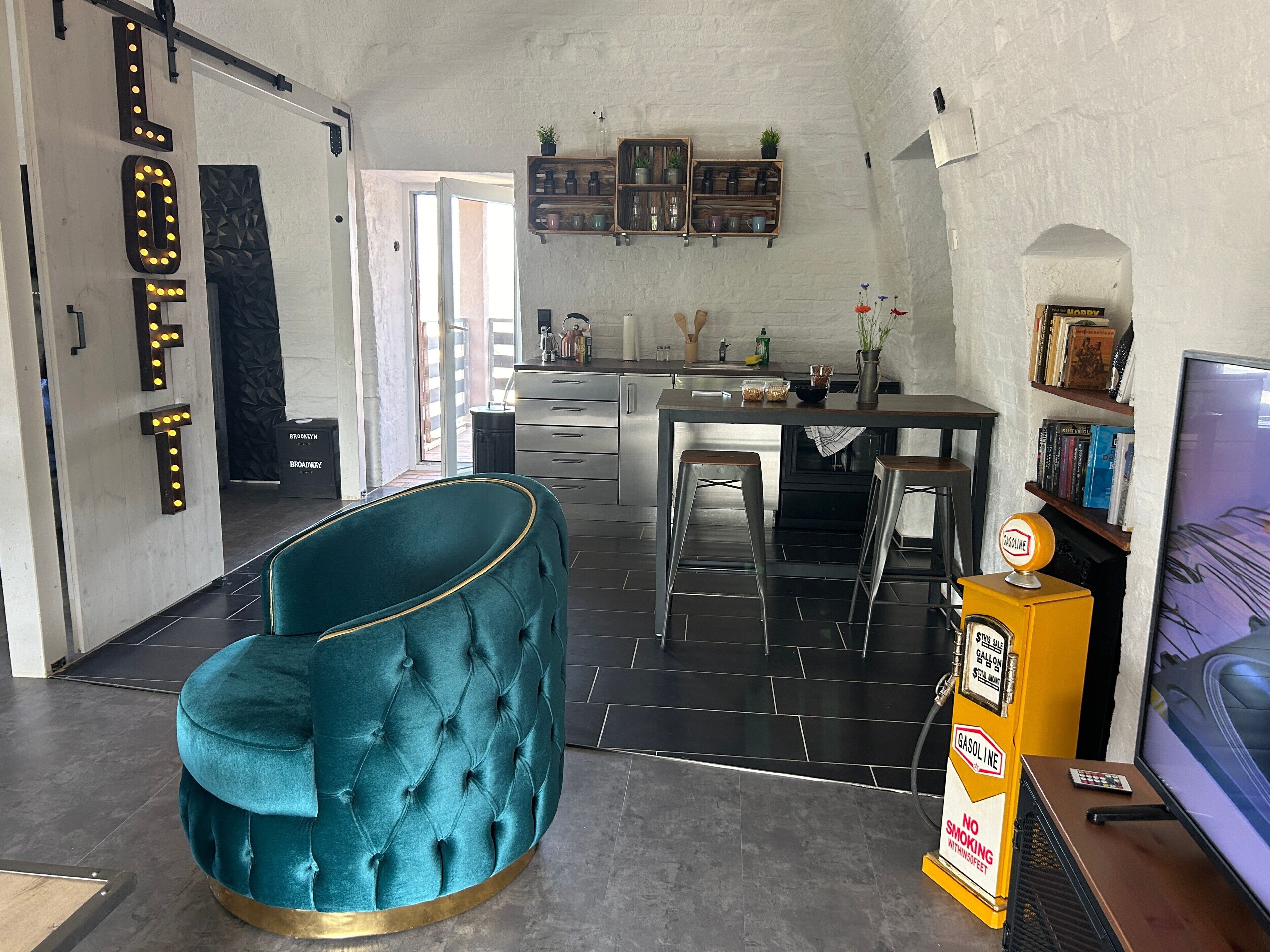 Une cuisine moderne avec un coin bar, un fauteuil recouvert d’un tissu de couleur turquoise et un téléviseur.