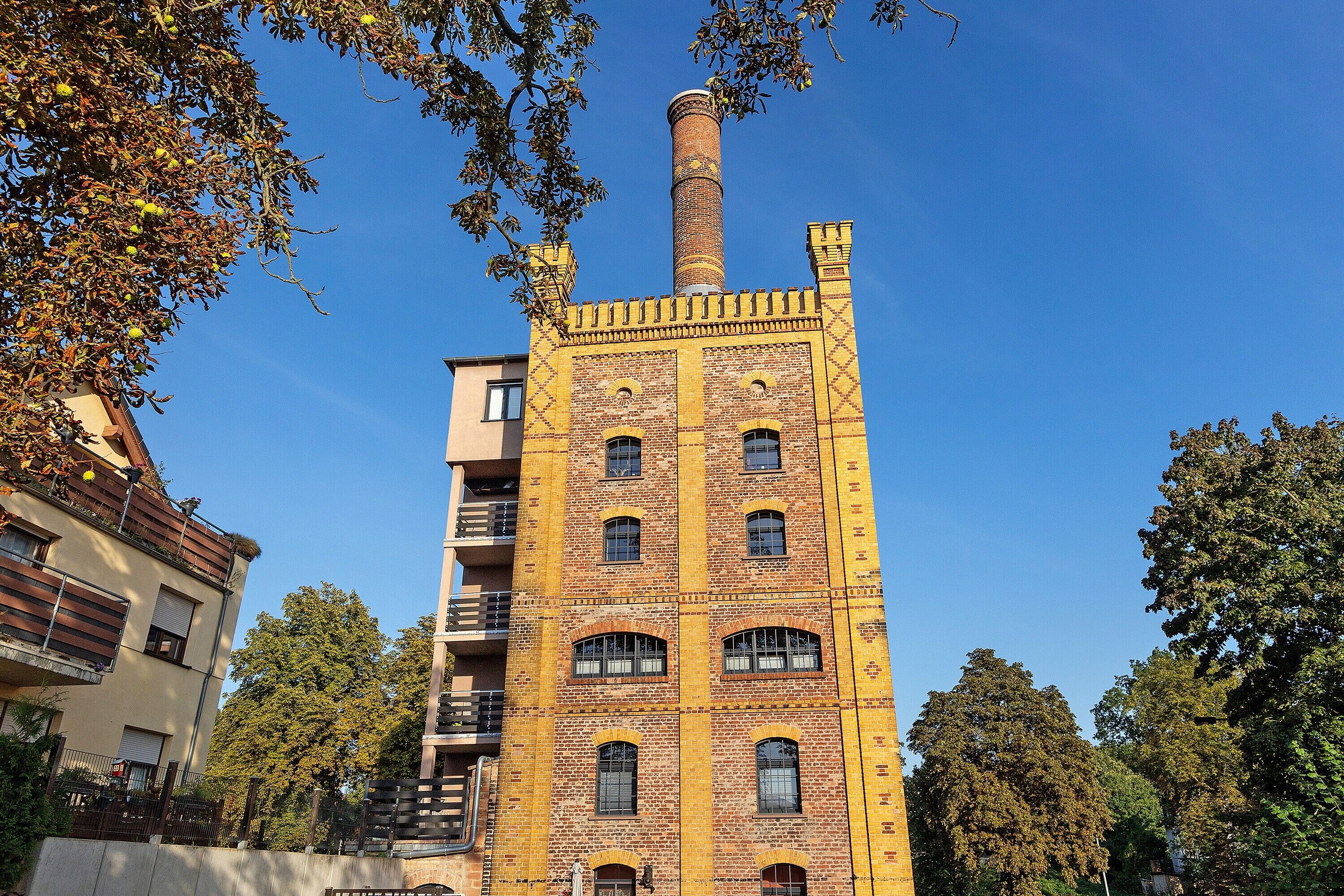Un grand bâtiment en briques, doté de nombreuses fenêtres et d’une cheminée, entouré d’arbres et d’autres bâtiments.