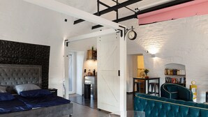 Ein modernes Wohnzimmer mit einer gepolsterten Couch, einem transparenten Glastisch und einem großen Bett mit Kopfteil.