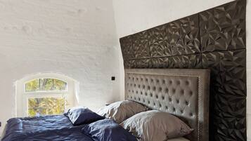 Une chambre à coucher avec une tête de lit capitonnée, une fenêtre donnant sur des arbres et un mur orné d’un motif géométrique.