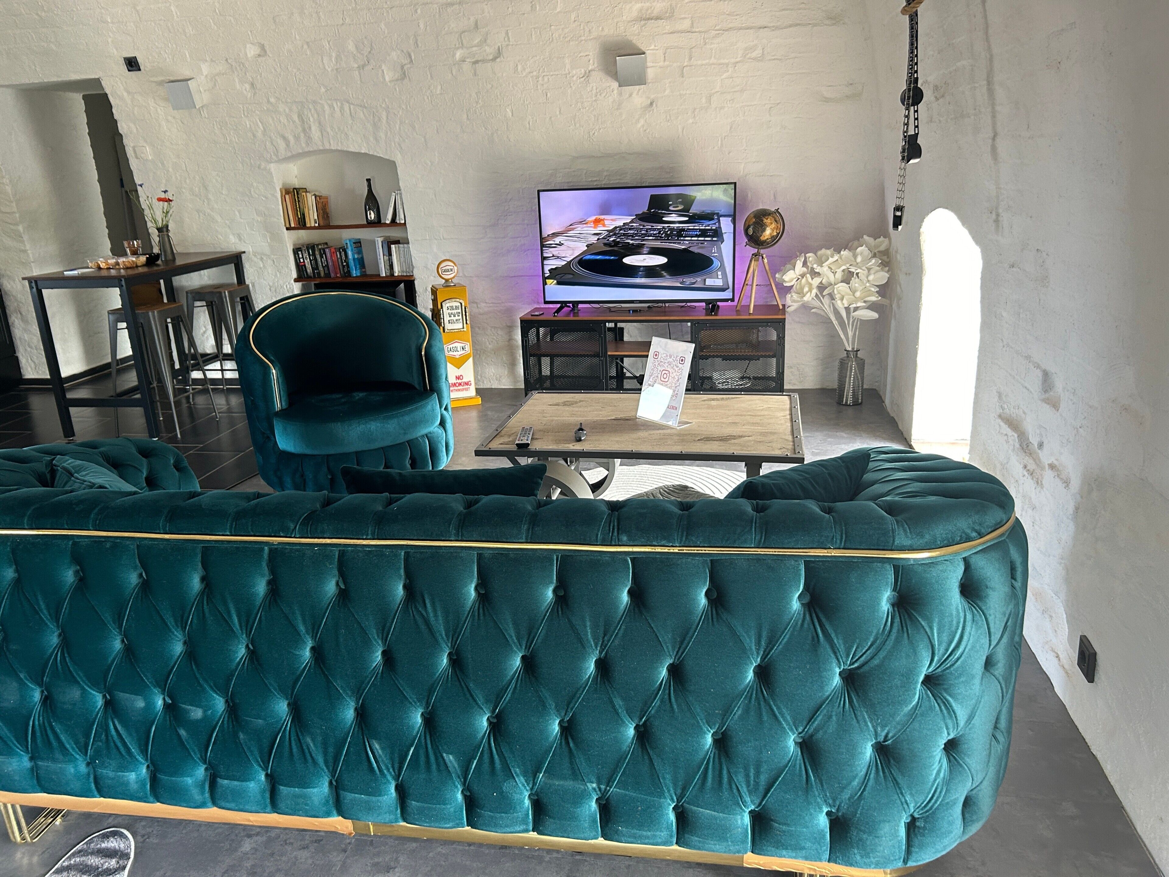 Ein smaragdgrünes Polstersofa, ein Fernseher und eine Bar mit einer weißen Ziegelwand.