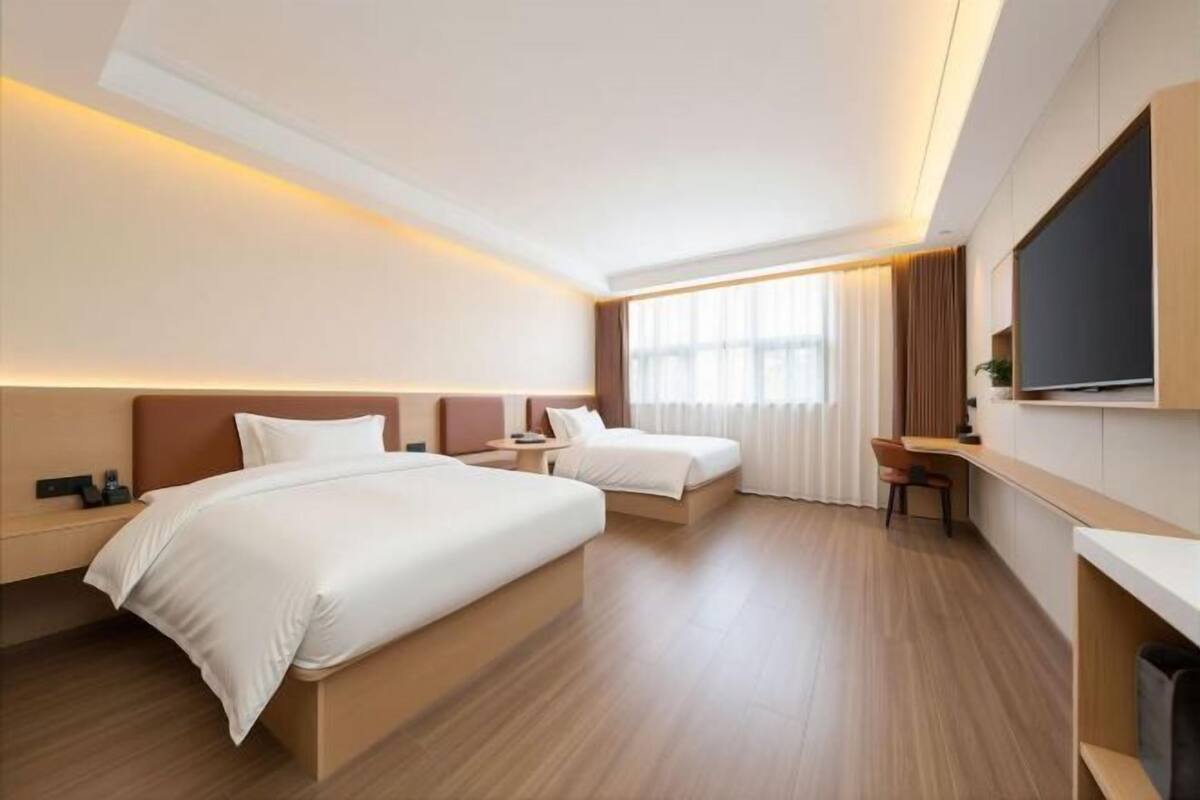 A hotel room with two beds, a desk, a chair, a TV, and a large window with curtains.