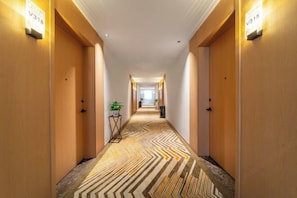 A hotel hallway with carpeted floors, wooden doors, and wall-mounted light fixtures.