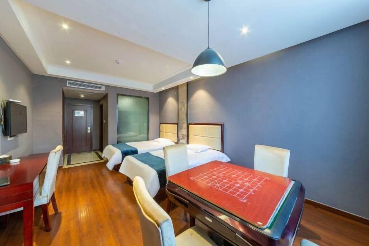 A hotel room with two beds, a desk, and a dining table.