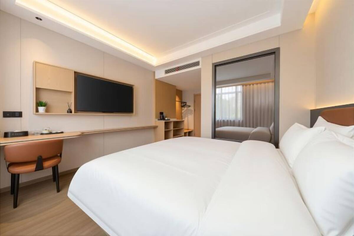 A hotel room with a bed, a desk, a chair, a TV, and a wardrobe.
