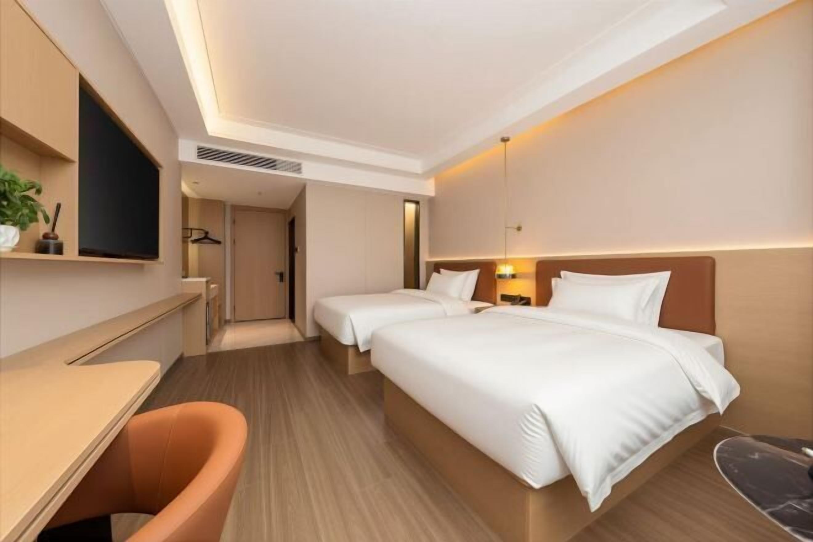 Ein Hotelzimmer mit Schreibtisch, zwei Betten, einem Sessel und einem Fernseher.