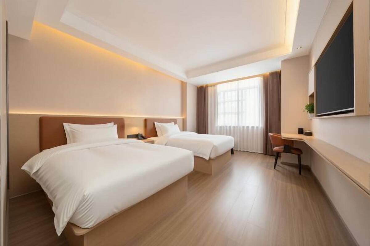 A hotel room with two beds, a desk, a chair, and a large window.