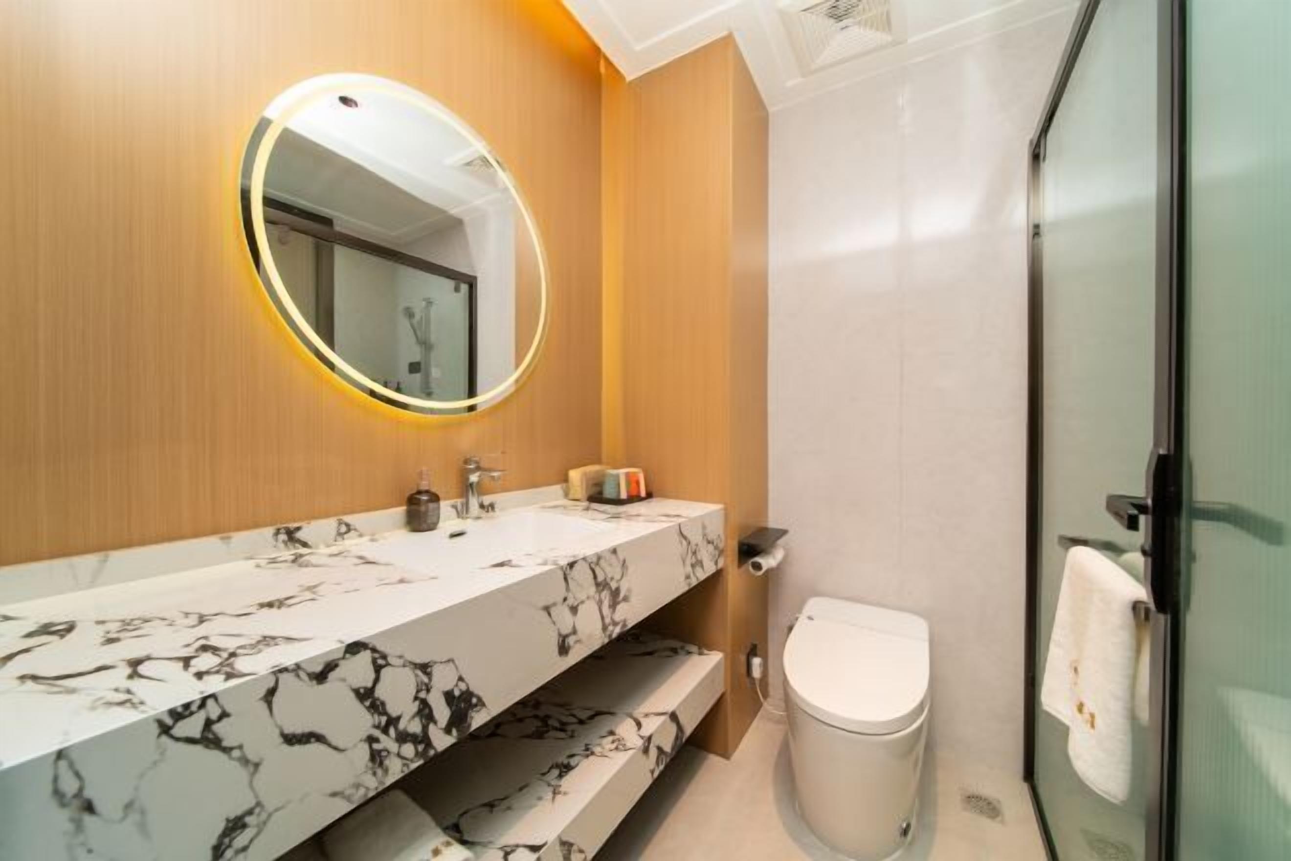 Une salle de bain avec un meuble-lavabo en marbre, un miroir rond, des toilettes et une cabine de douche en verre.