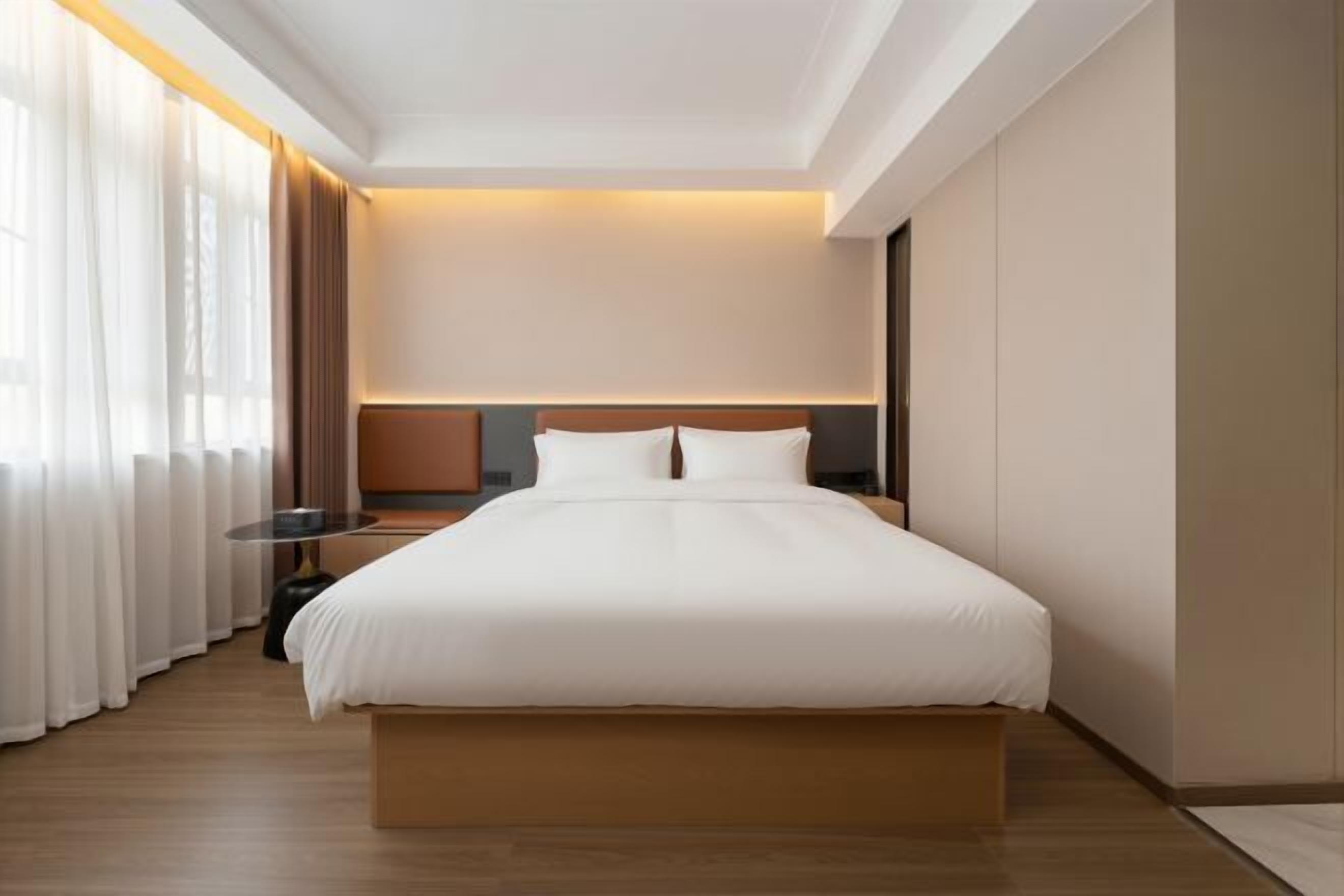 Quarto de hotel com uma cama grande, uma mesa de cabeceira, uma luminária e vista para o exterior.