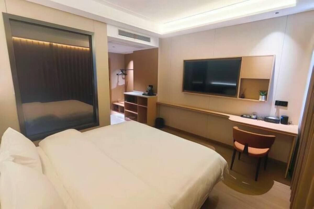 A hotel room with a bed, a desk, a chair, a television, and a wardrobe.