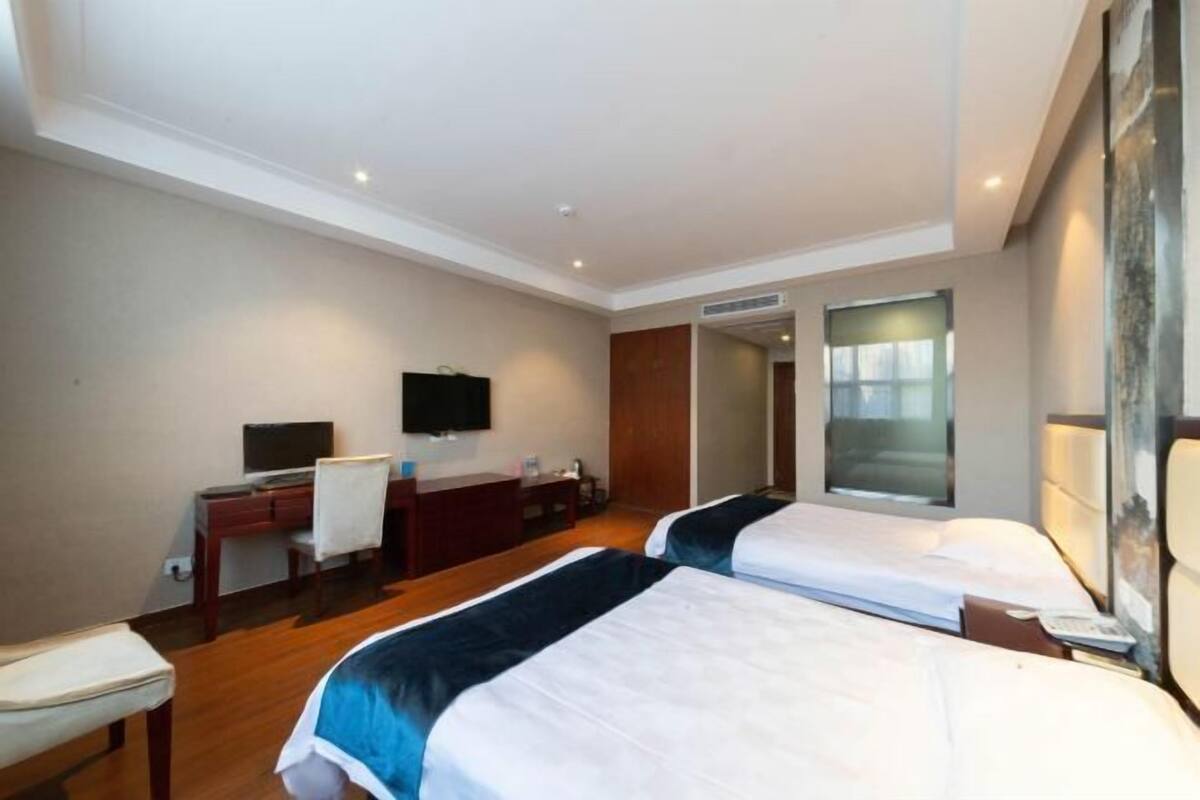 A hotel room with two beds, a desk, a chair, a TV, and a large window.