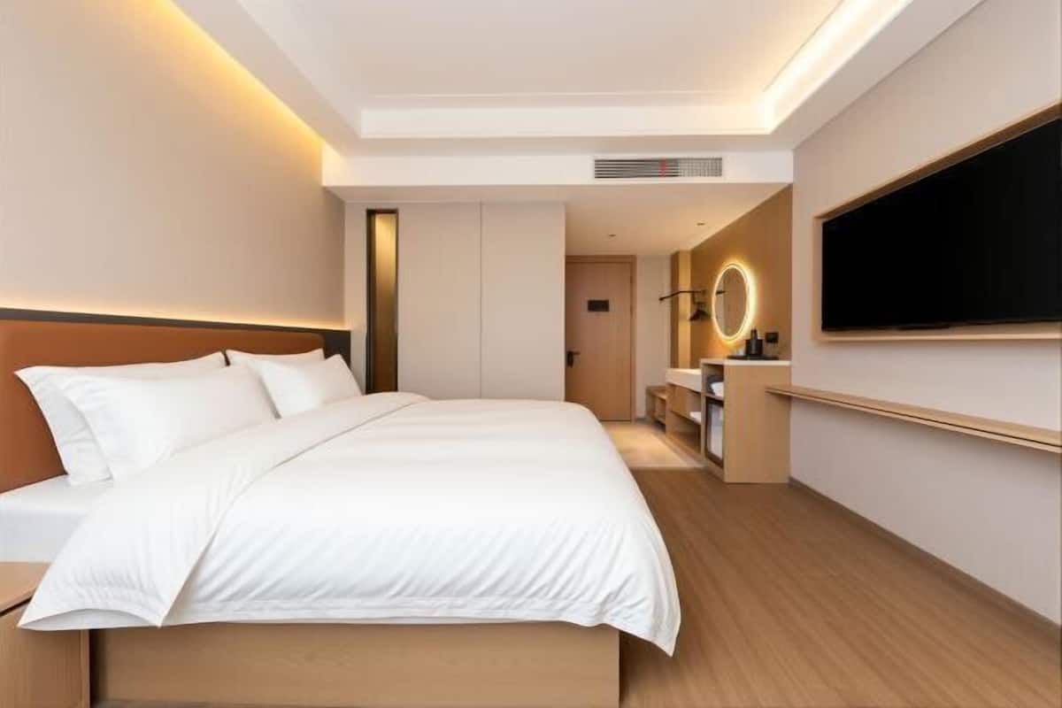A modern hotel room with a large bed, a TV mounted on the wall, and a small desk with a mirror.