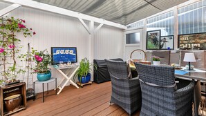 A covered outdoor area with wicker furniture, a TV, potted plants, and a window.