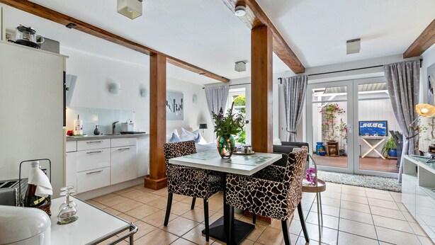 A modern kitchen with white cabinets, a dining table with patterned chairs, and a view of the outside through glass doors.