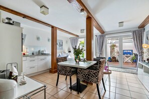 Une cuisine moderne avec des meubles blancs, une table à manger entourée de chaises à motifs et une vue sur l’extérieur grâce à des portes vitrées.