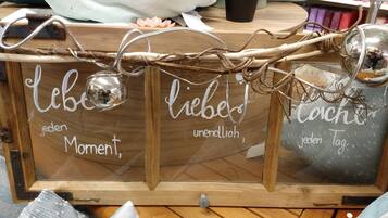 Una vitrina de madera con la inscripción 'Liebe jeden Moment, liebe jeden Tag' y elementos decorativos como ramas y una planta pequeña.