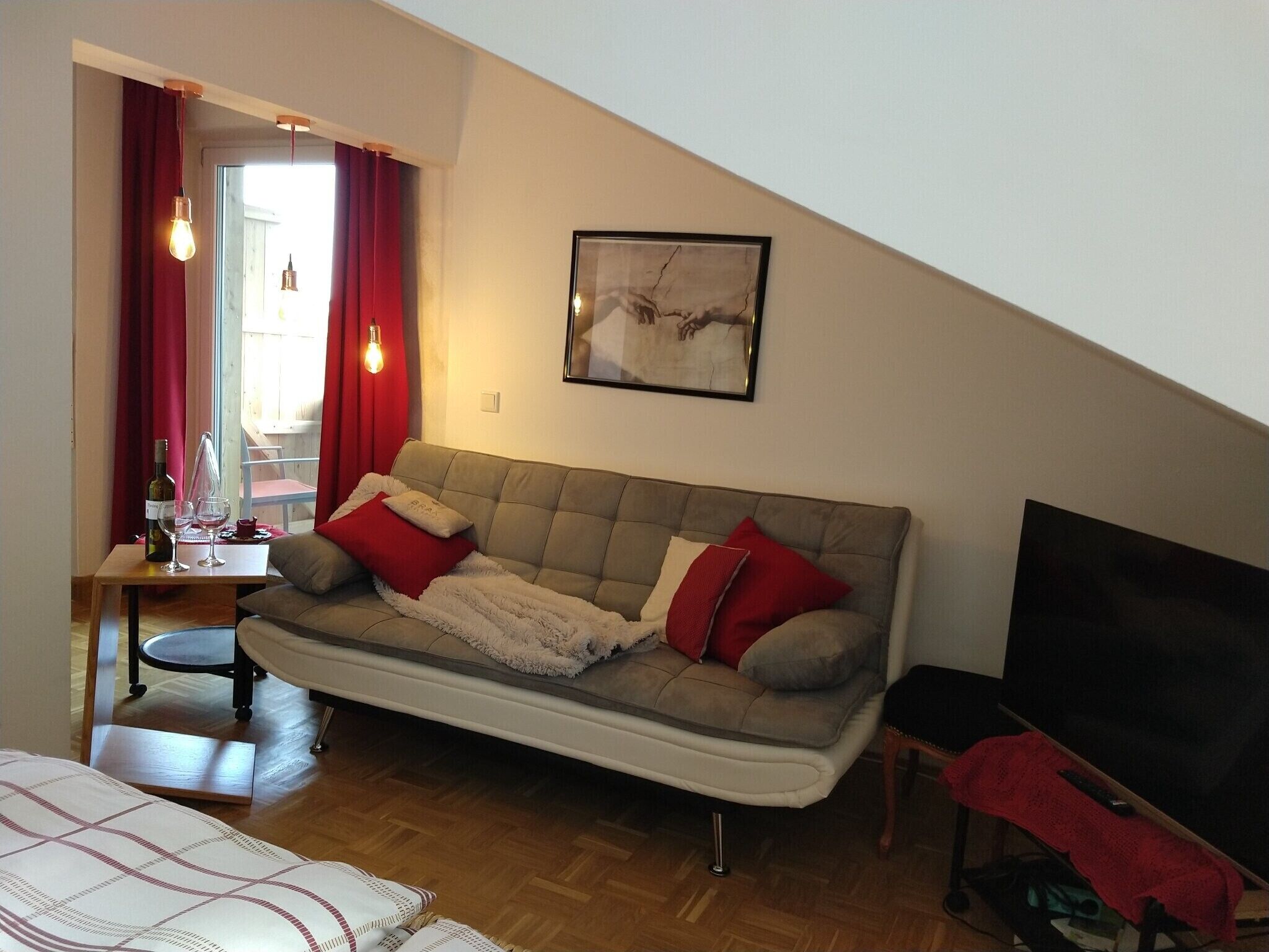 En stue med sofa, et bord med vinglas, et fjernsyn og et billede på væggen.