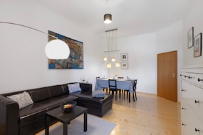 Un salon moderne avec un canapé, une table basse, une table à manger et des chaises. Il y a un tableau au mur et une porte en bois.