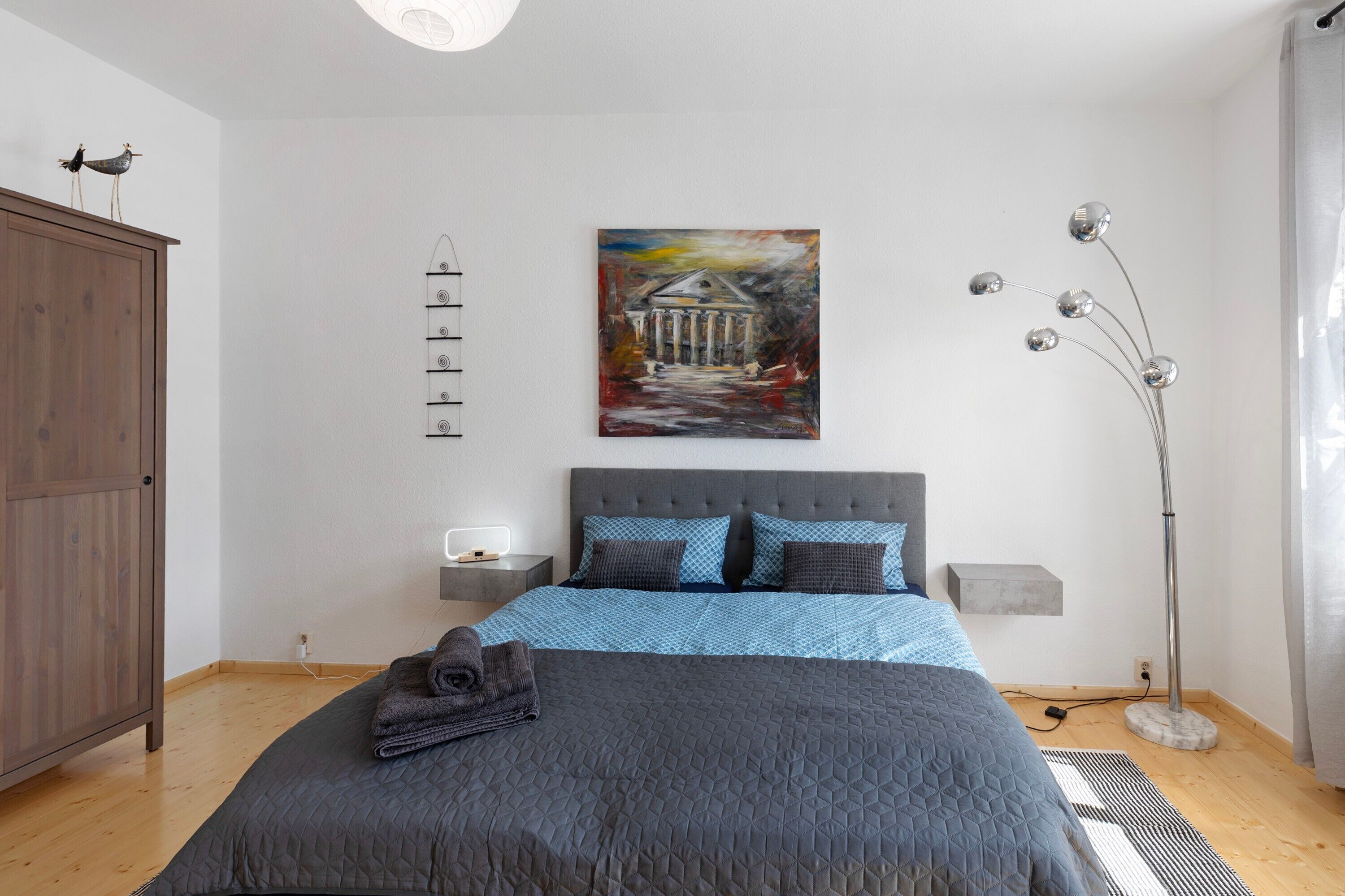 Een slaapkamer met een bed, een schilderij, een kledingkast en een vloerlamp.