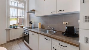 A modern kitchen with white cabinets, a stainless steel sink, a built-in oven, and a window with curtains.