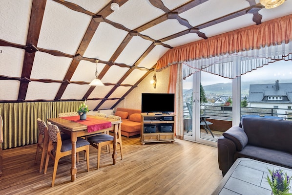 Un salon chaleureux avec un plafond en bois, un téléviseur à écran plat, un canapé et une table à manger avec des chaises.