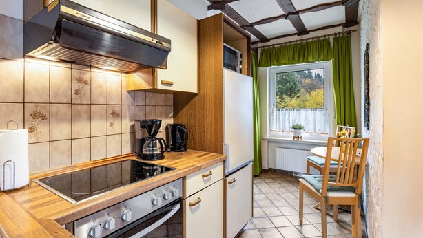 Une cuisine compacte équipée d’une cuisinière, d’un four et d’une machine à café, de placards en bois et d’une fenêtre avec des rideaux.