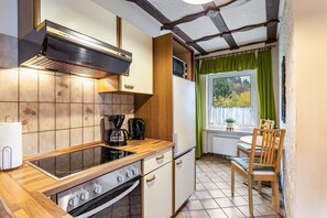 Une cuisine compacte équipée d’une cuisinière, d’un four et d’une machine à café, de placards en bois et d’une fenêtre avec des rideaux.