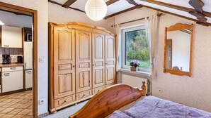 Ein Schlafzimmer mit einem hölzernen Bett, einem Kleiderschrank, einem Fenster mit Blick auf Grünflächen und einem Spiegel an der Wand.