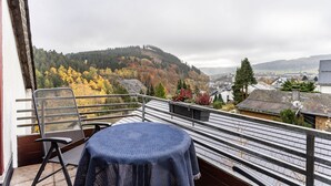 Ein Balkon mit Tisch und Stuhl, der einen Blick auf einen Hügel mit Herbstlaub und eine darunterliegende Stadt bietet.