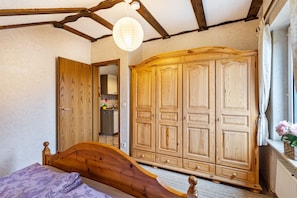 Une chambre avec un lit en bois, une armoire, une fenêtre donnant sur un beau paysage et un luminaire suspendu.