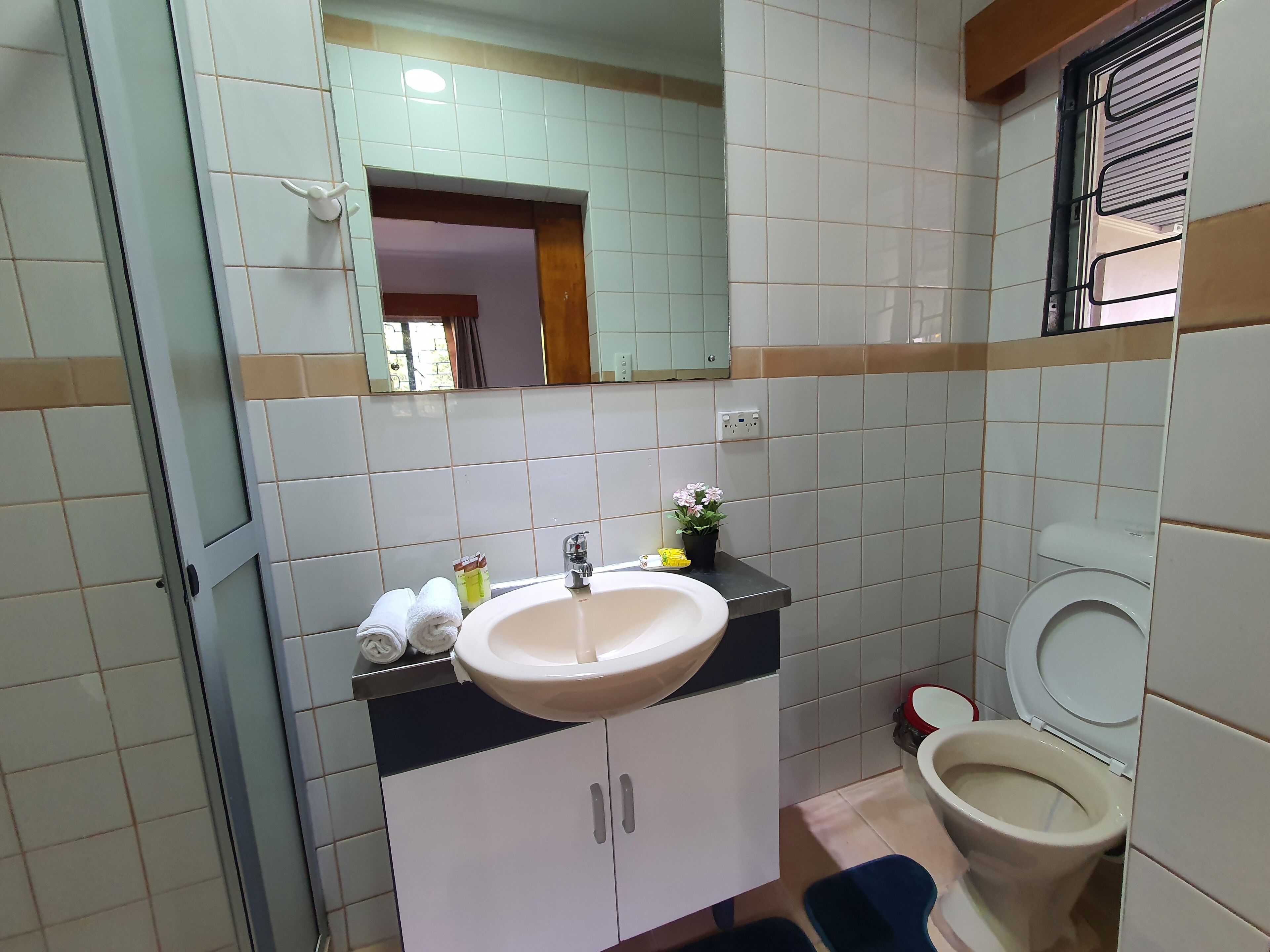 Une salle de bain avec un lavabo, un miroir, des toilettes et une petite fenêtre.